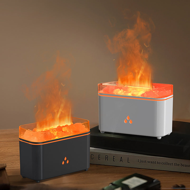 Two tabletop electric flame lamps with glowing orange faux flames and illuminated crystal stones, shown on a wooden surface with one placed in front and one resting on a book in the background.