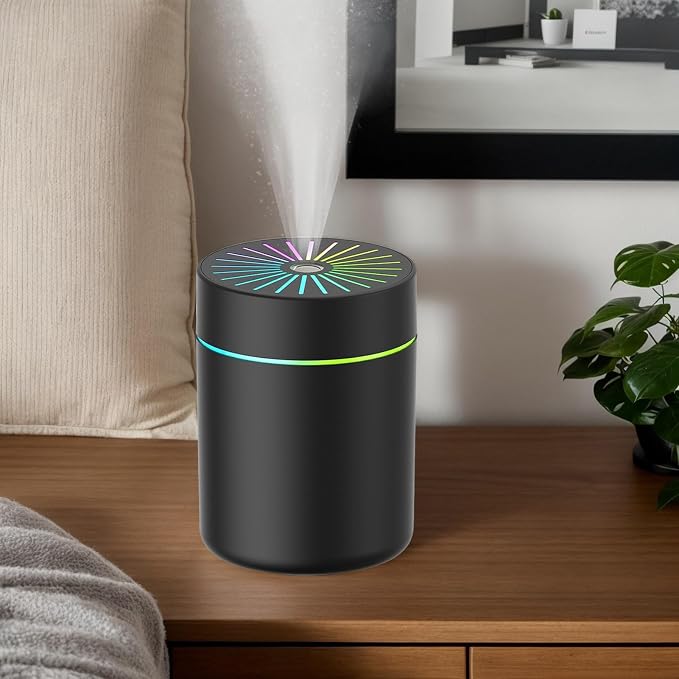 A black cylindrical humidifier with a glowing multicolor LED ring sits on a wooden table in a modern living room setting, with mist visibly spraying from the top.