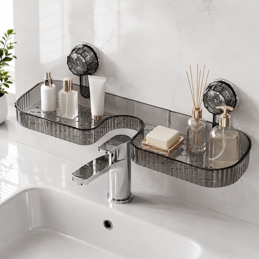 Two dark gray translucent acrylic bathroom wall shelves mounted above a white sink with a chrome faucet. The shelves are styled with toiletries, a soap dish, a reed diffuser, and a small plant is visible on the left against a white marble-look tiled wall.