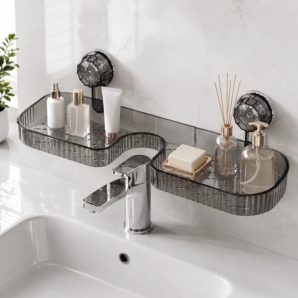 Two dark gray translucent acrylic bathroom wall shelves mounted above a white sink with a chrome faucet. The shelves are styled with toiletries, a soap dish, a reed diffuser, and a small plant is visible on the left against a white marble-look tiled wall.