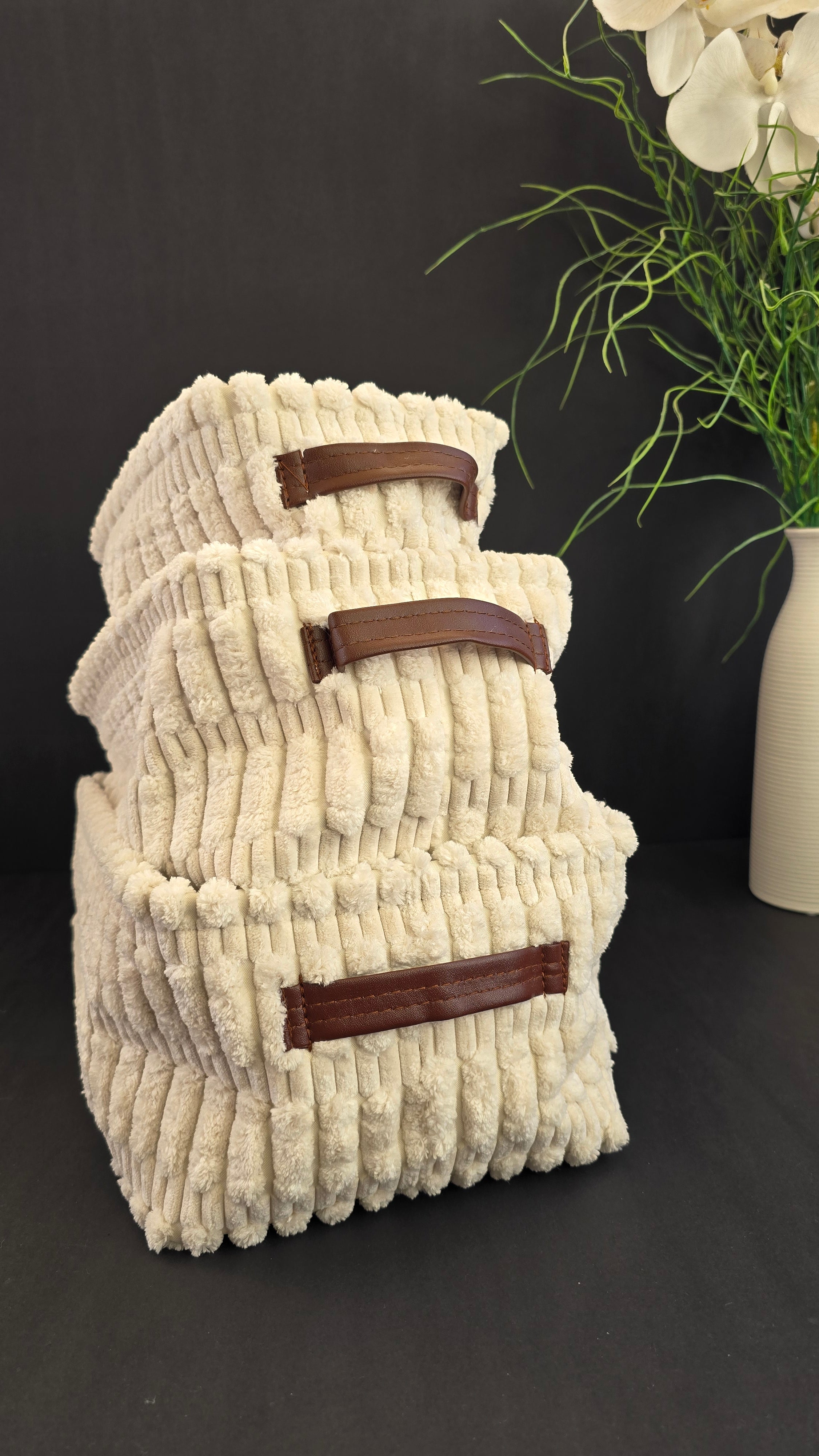 Three cream textured fabric storage baskets in graduated sizes with brown handles