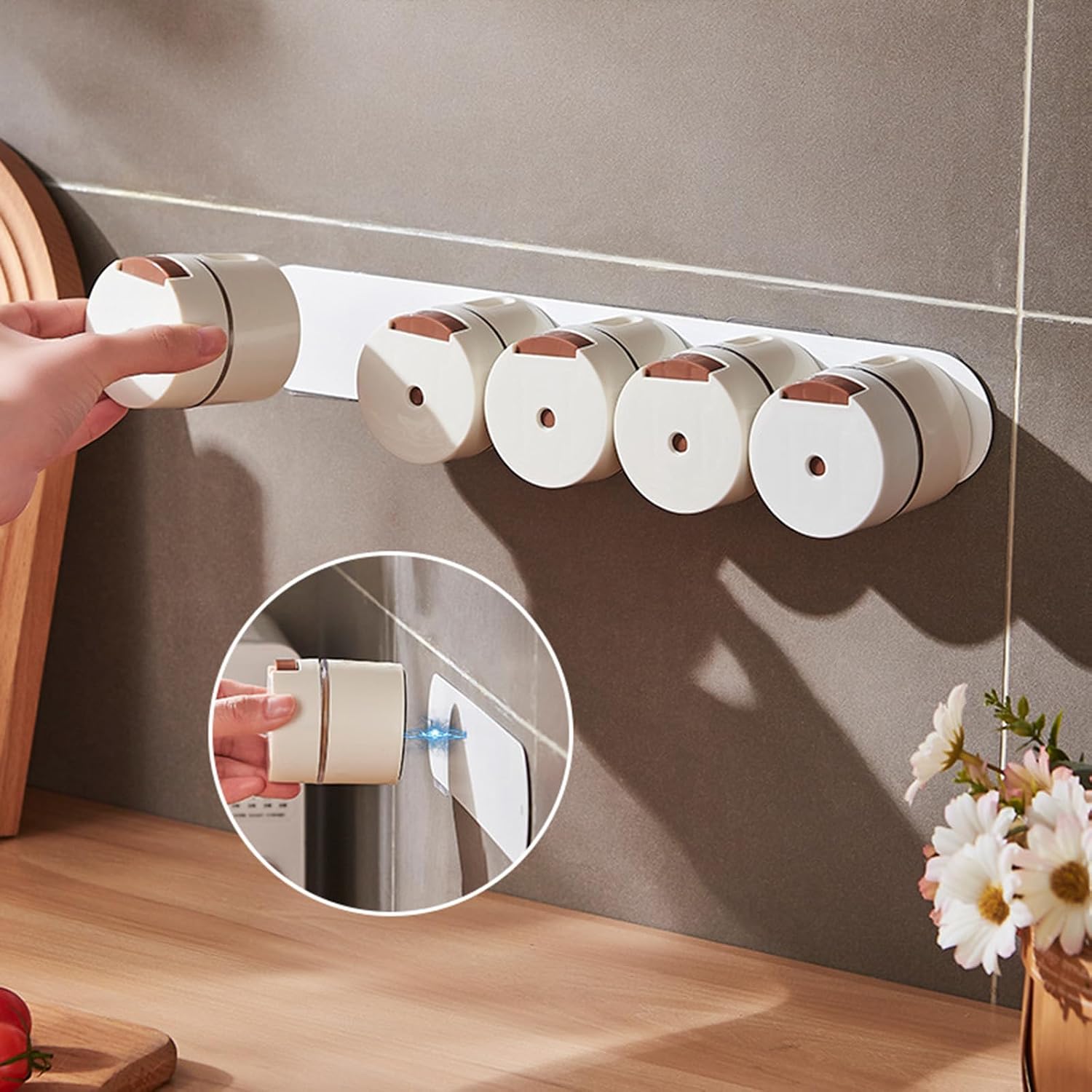 A set of six white cylindrical wall-mounted dispenser holders with rose gold accents, mounted on a gray tiled wall above a wooden countertop. A hand is shown interacting with the leftmost dispenser, and a circular inset demonstrates how one of the dispensers is attached.