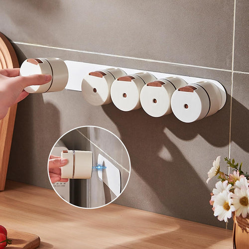 A set of six white cylindrical wall-mounted dispenser holders with rose gold accents, mounted on a gray tiled wall above a wooden countertop. A hand is shown interacting with the leftmost dispenser, and a circular inset demonstrates how one of the dispensers is attached.