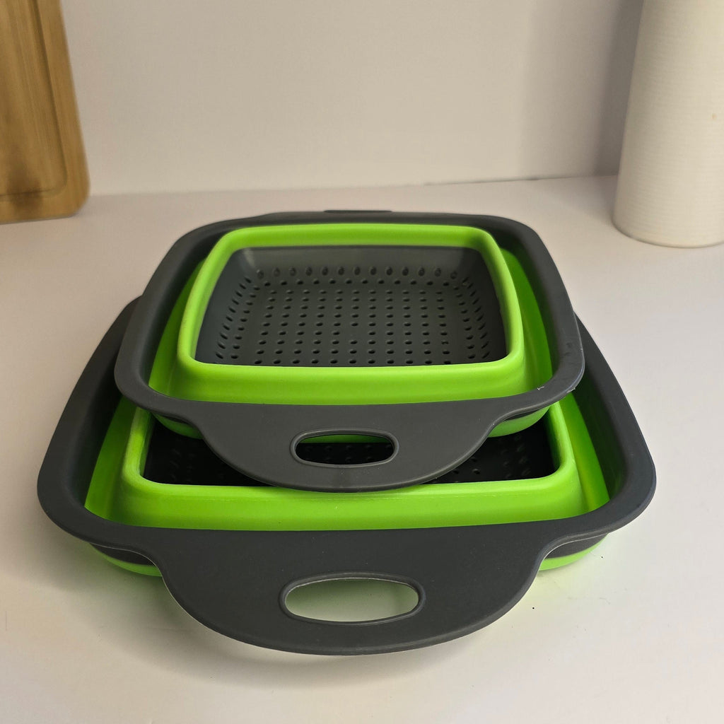 Three nested square silicone colanders in lime green and dark gray, stacked on a white tabletop with a neutral indoor background.