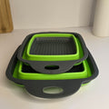 Three nested square silicone colanders in lime green and dark gray, stacked on a white tabletop with a neutral indoor background.