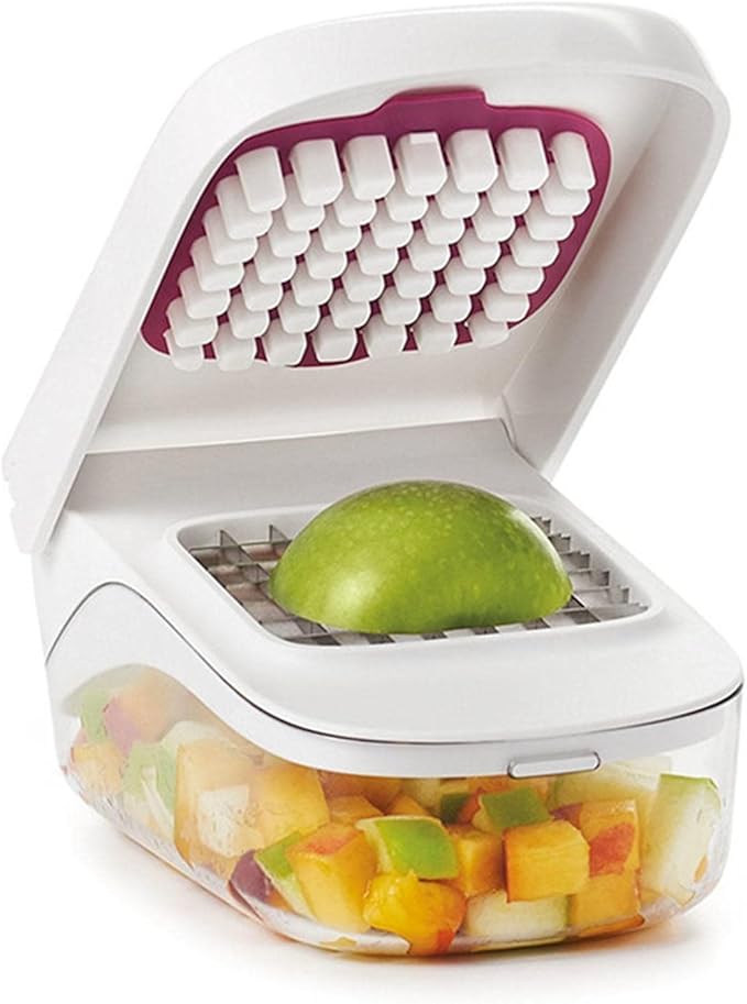 A white plastic fruit chopper and dicer with a clear container holding chopped fruit pieces. An apple is shown being processed in the center slot, and the inside lid features white cutting teeth over a magenta accent.