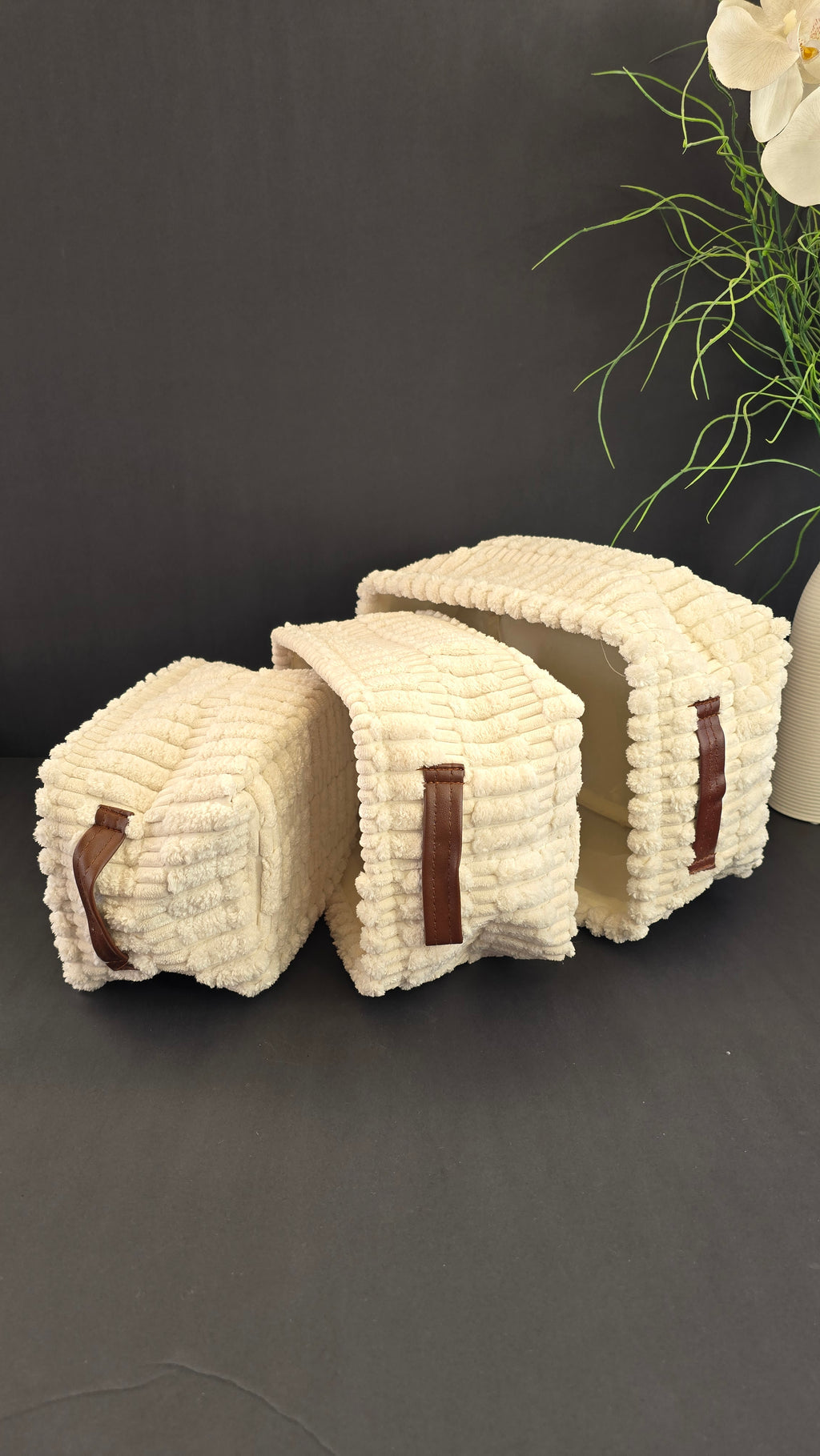 Three cream fabric storage baskets stacked to show their brown carrying handles