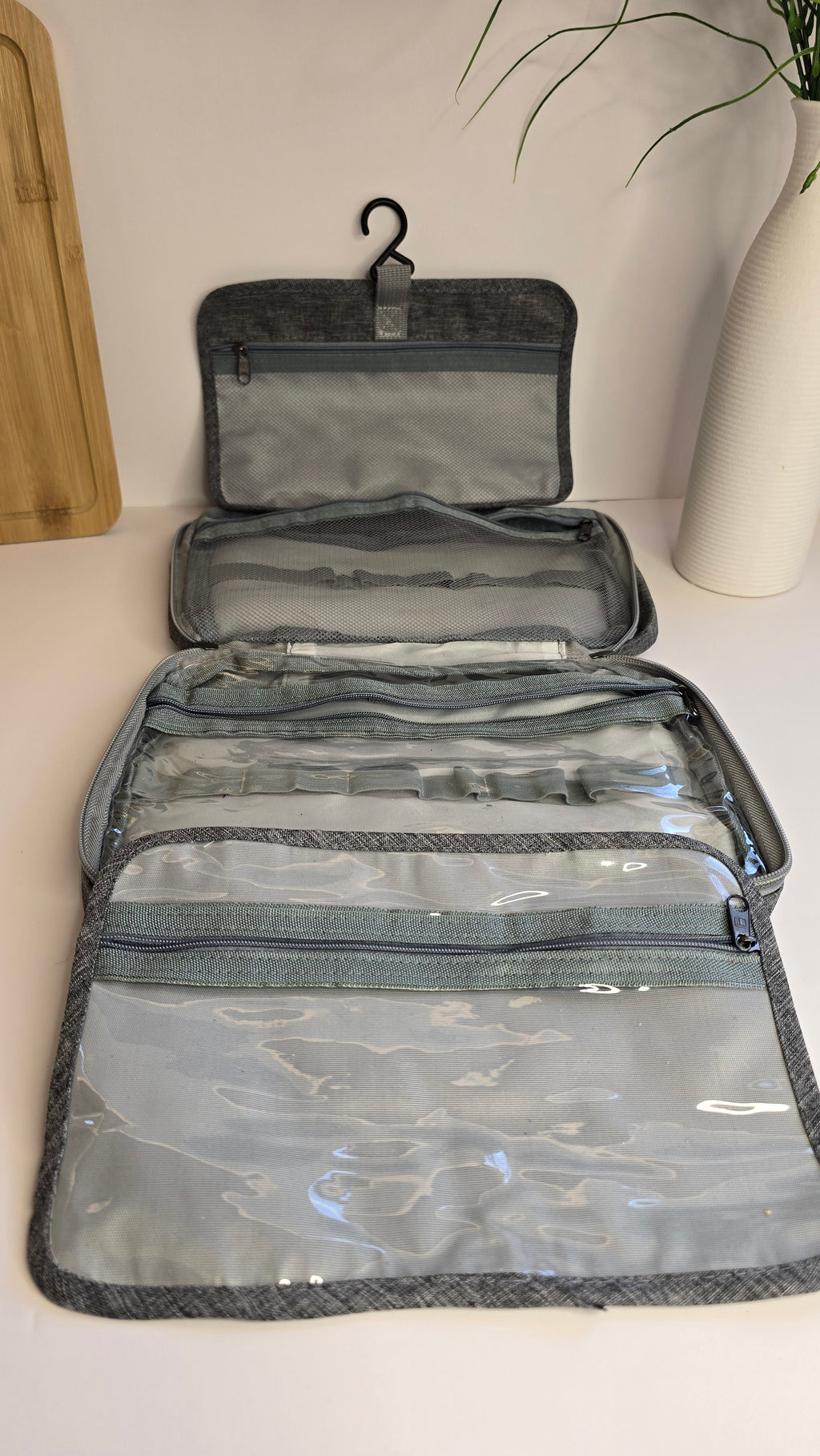 Gray and clear waterproof travel organizer pouches shown open on a white surface, with a wooden board and plant visible in the background.