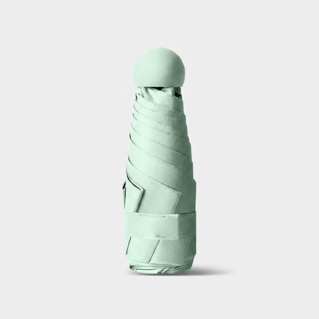 A folded compact umbrella in a pale mint green color, standing upright on a light gray background.