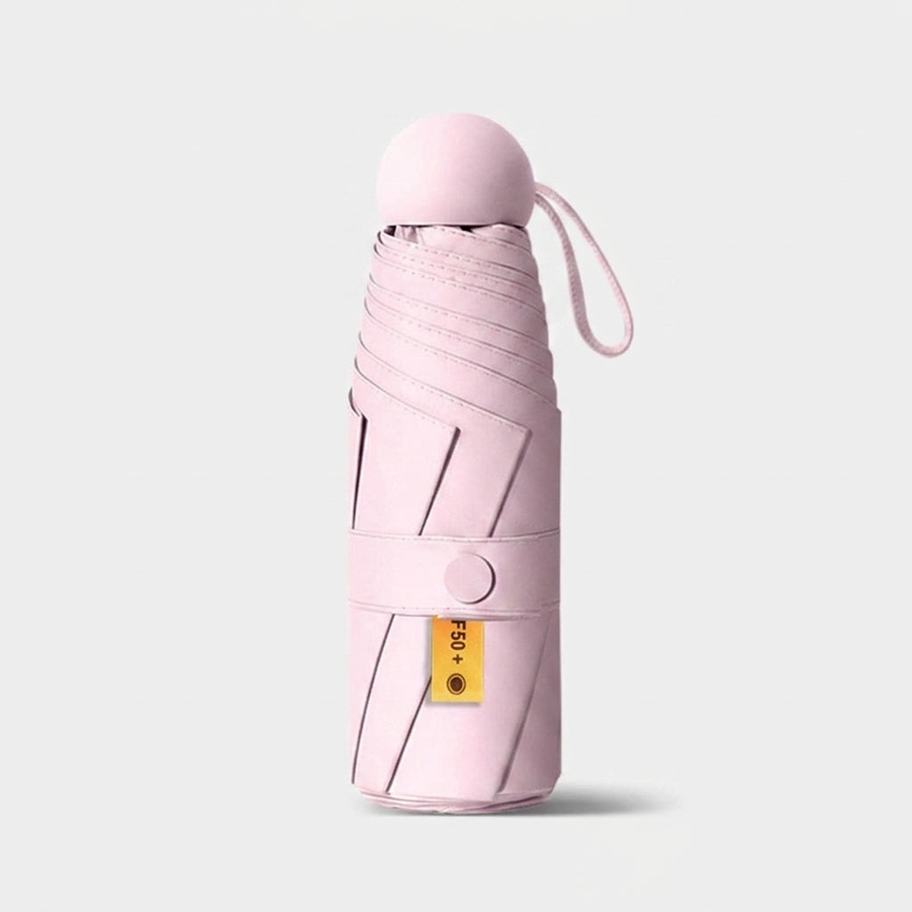 A folded light pink umbrella in a sleek cylindrical case with a matching pink cap and wrist loop, shown on a clean light gray background.