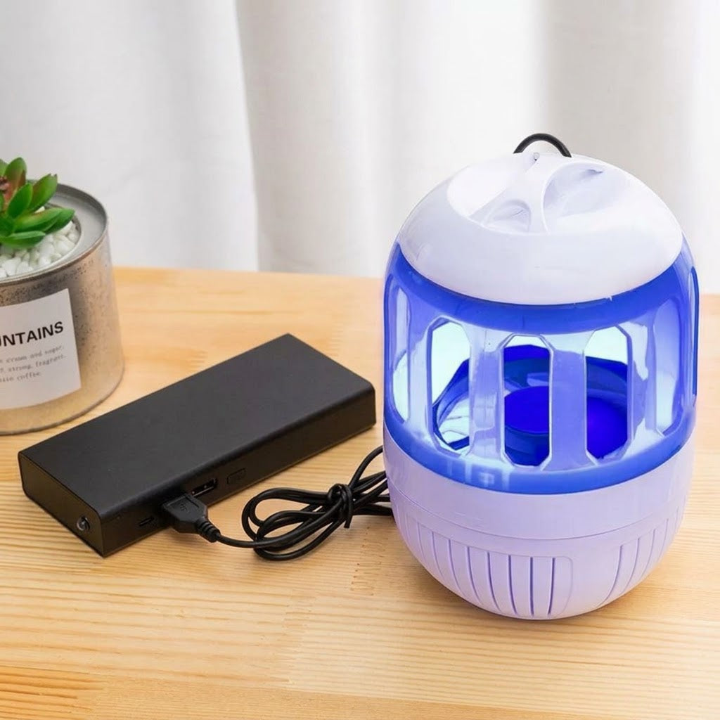 A blue and white electronic insect trap or mosquito killer sits on a wooden table next to its black power adapter, with a small potted succulent in the background.