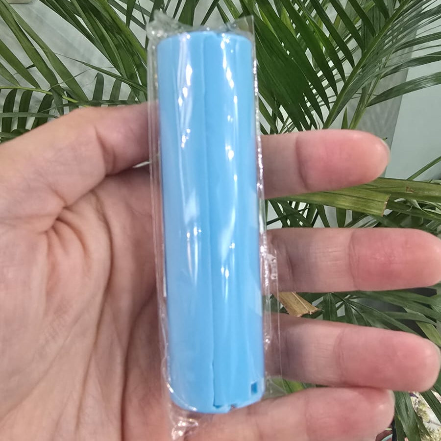 A hand holding a light blue cylindrical plastic item wrapped in clear plastic packaging, with a green potted plant in the background.