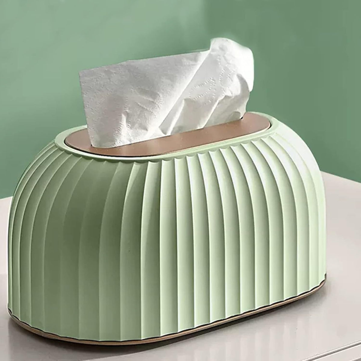 A mint green pleated tissue box cover with a white tissue paper partially pulled out, set on a white surface against a matching green background.