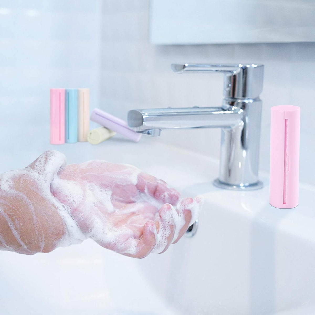 A close-up of a person's foamy hands at a bathroom sink with a chrome faucet, alongside pink and pastel soap bars.