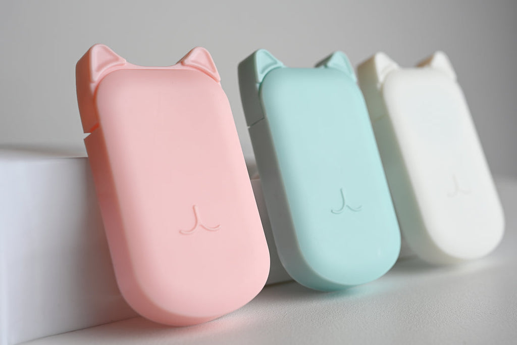 Three cat-shaped portable power banks in pastel pink, mint green, and white, arranged side-by-side on a light gray surface.