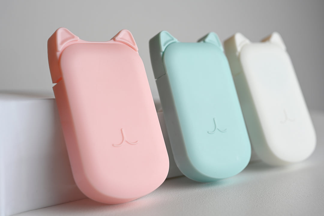 Three cat-shaped portable power banks in pastel pink, mint green, and white, arranged side-by-side on a light gray surface.