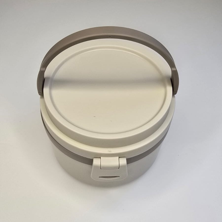 A round plastic lunch box with a light beige lid and handle, set against a plain white background.